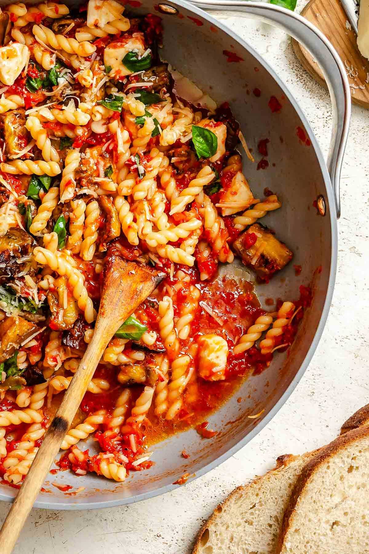 Saucy twisted pasta with chunks of roasted eggplant, melted mozzarella, and basil leaves in a gray skillet, highlighting the rich red sauce and tender vegetables.