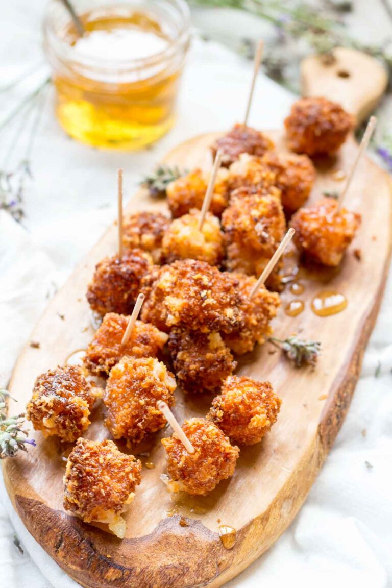 Full board of fried Manchego bites – A wooden board filled with fried Manchego cheese, lavender sprigs, and drizzled honey, with a jar of infused honey in the background.