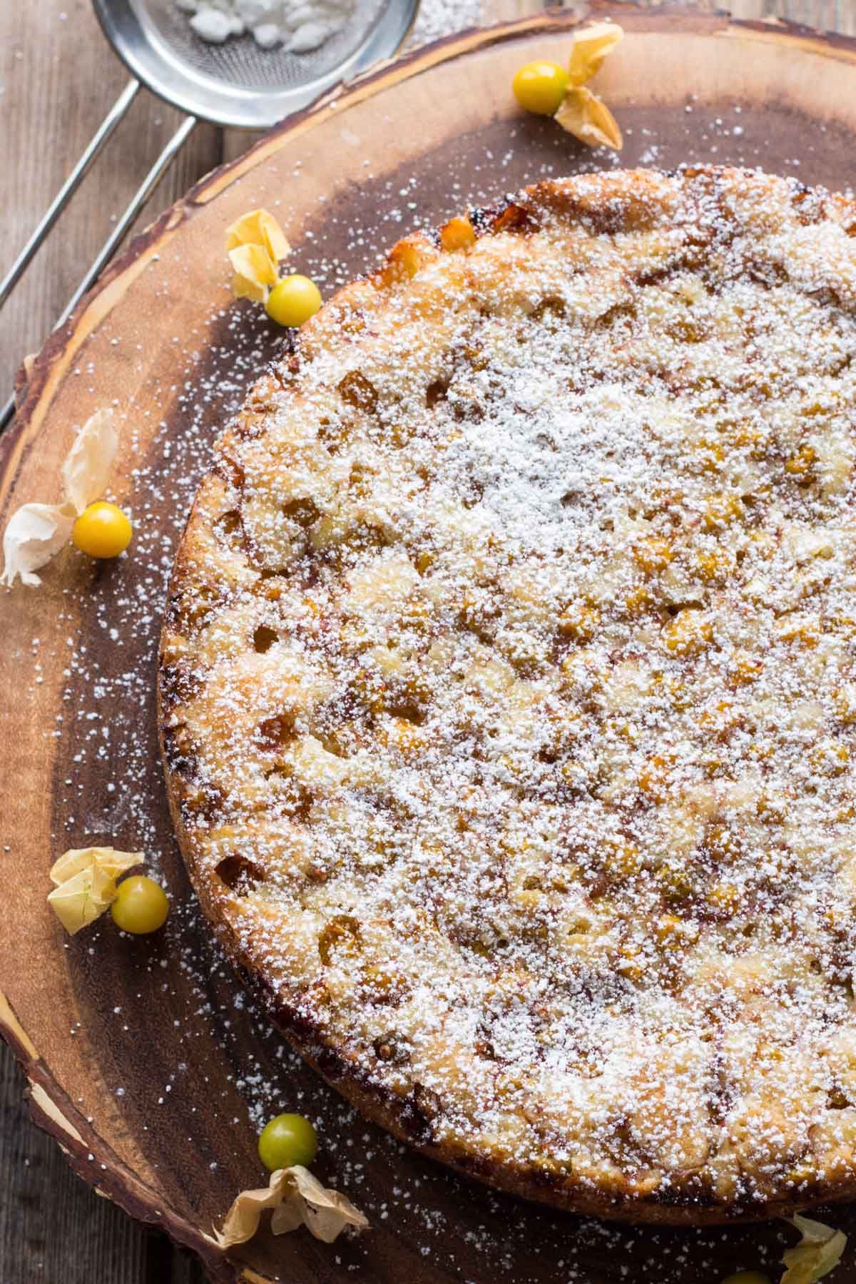Overhead view of the cake covered in powdered sugar, surrounded by scattered ground cherries and husks on the board.