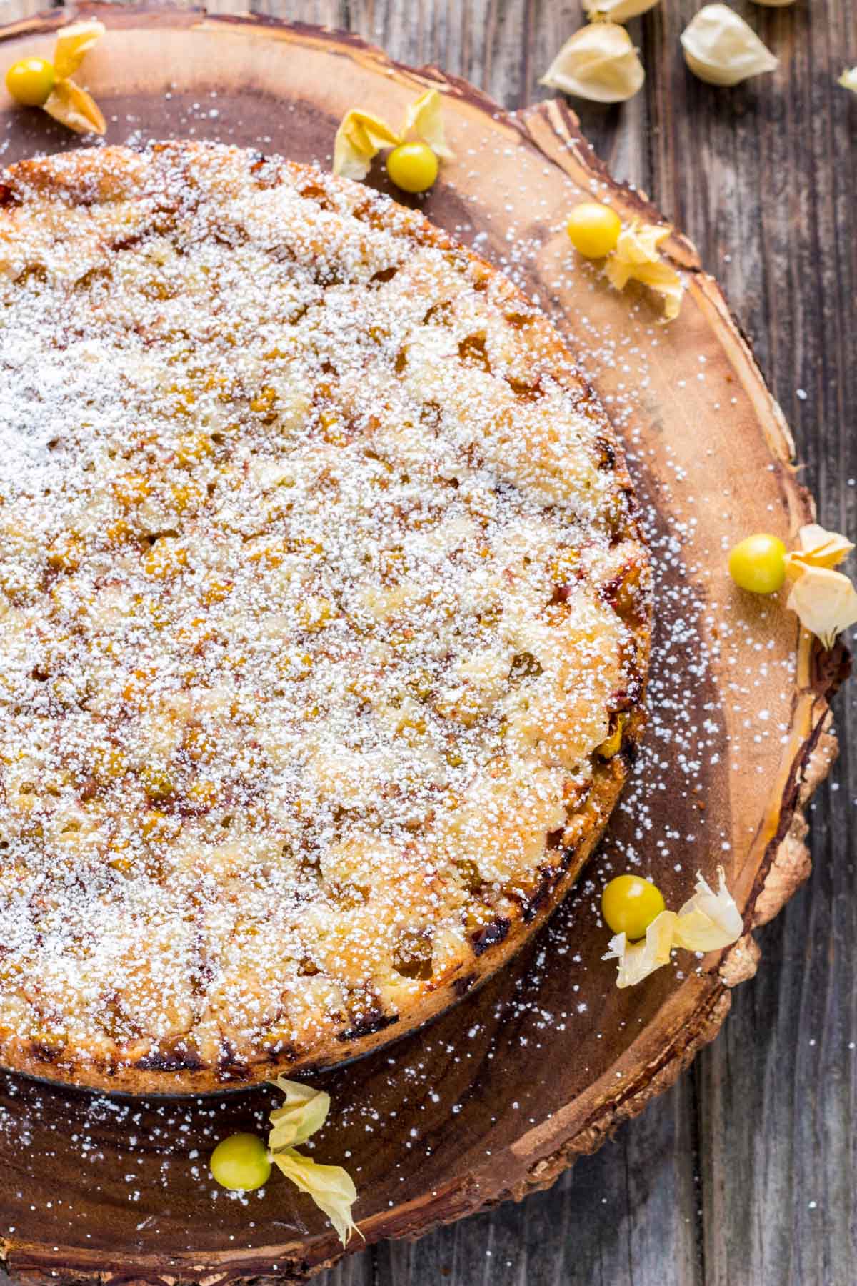Cake dusted generously with powdered sugar, decorated with scattered ground cherries around the rustic wood serving board.