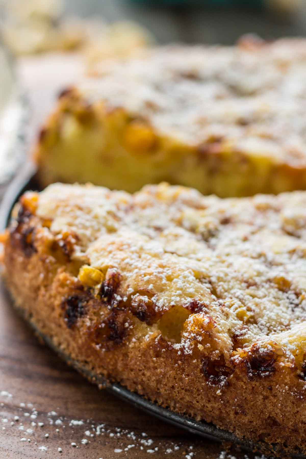 Close-up side view of the cake showing its golden crust and caramelized fruit on the edges, sprinkled with powdered sugar.