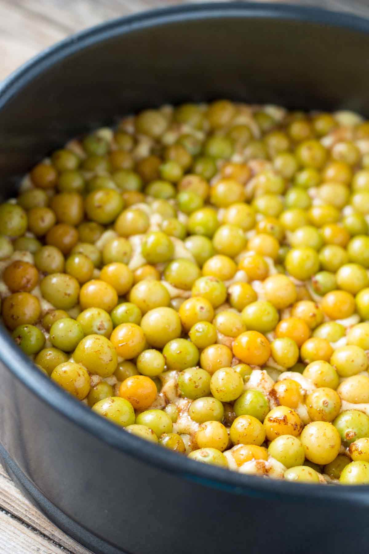 A cake pan filled with raw ground cherries mixed with cinnamon and sugar, ready to be baked.