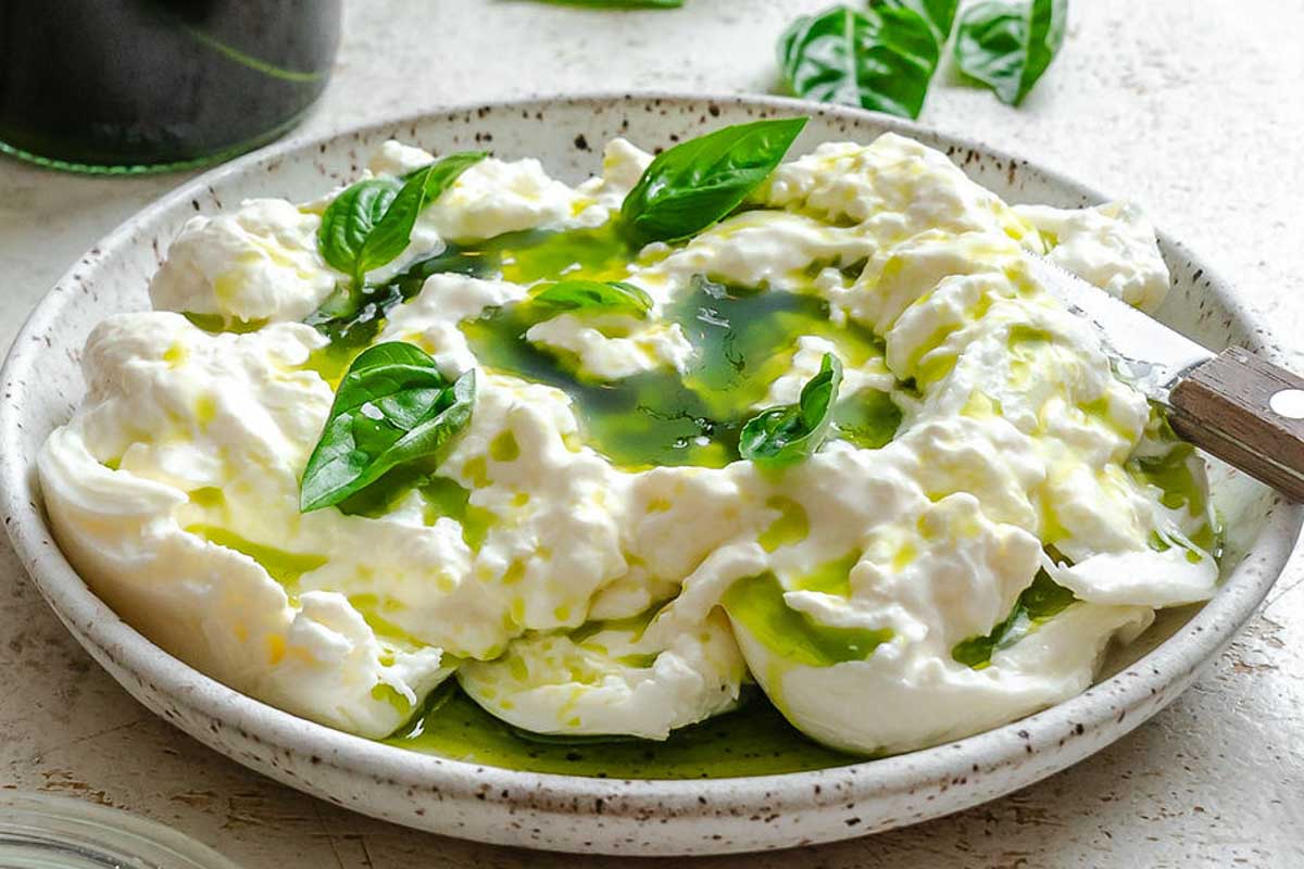 Close-up of burrata topped with glossy basil oil and fresh basil leaves.