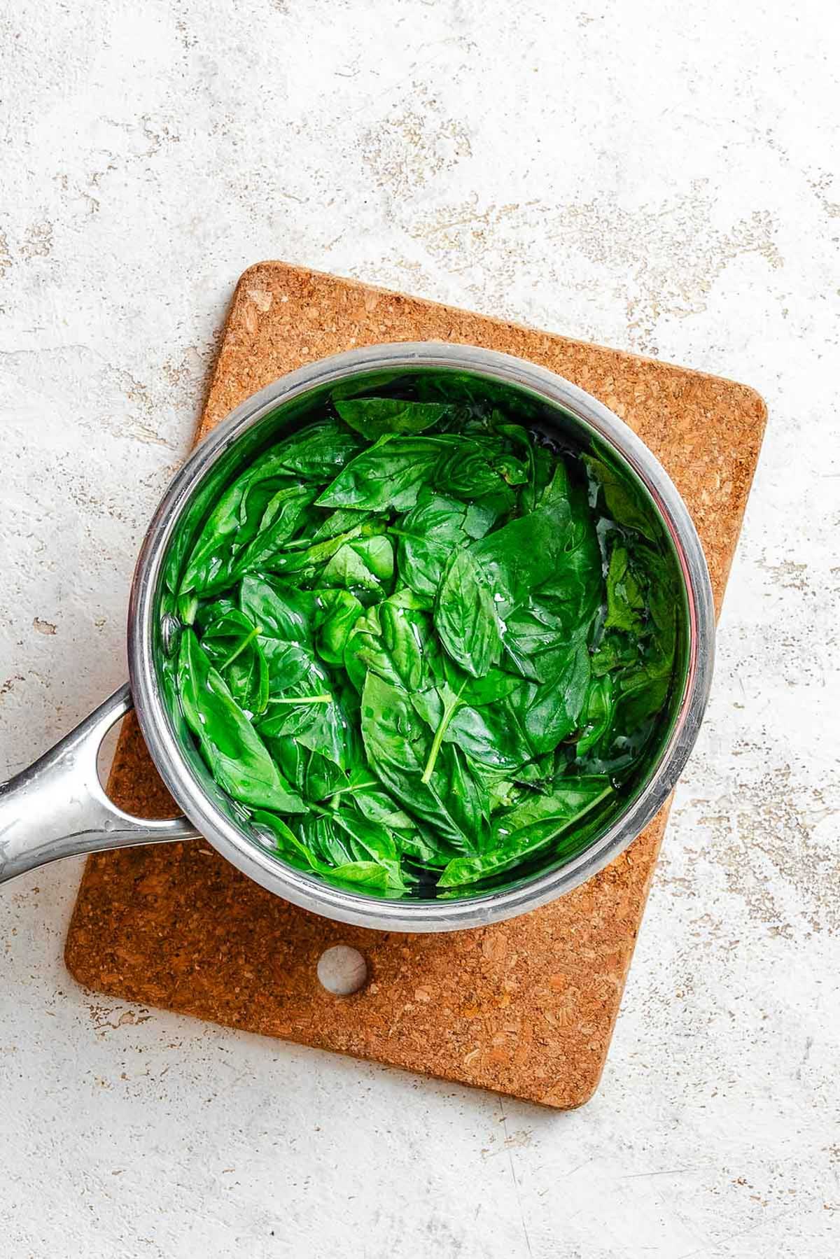 Blanching basil leaves in a stainless steel pot of salted water, the leaves bright green and fully submerged.