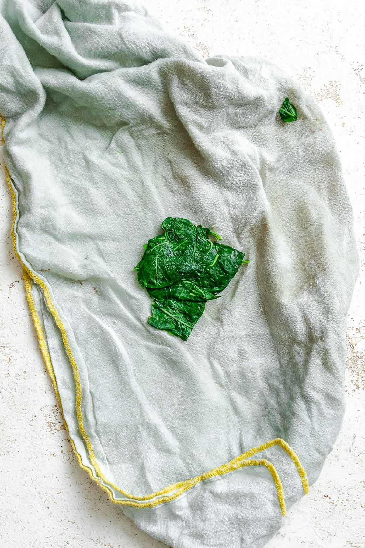 Draining basil leaves on a soft kitchen towel, excess moisture being removed after the ice bath.