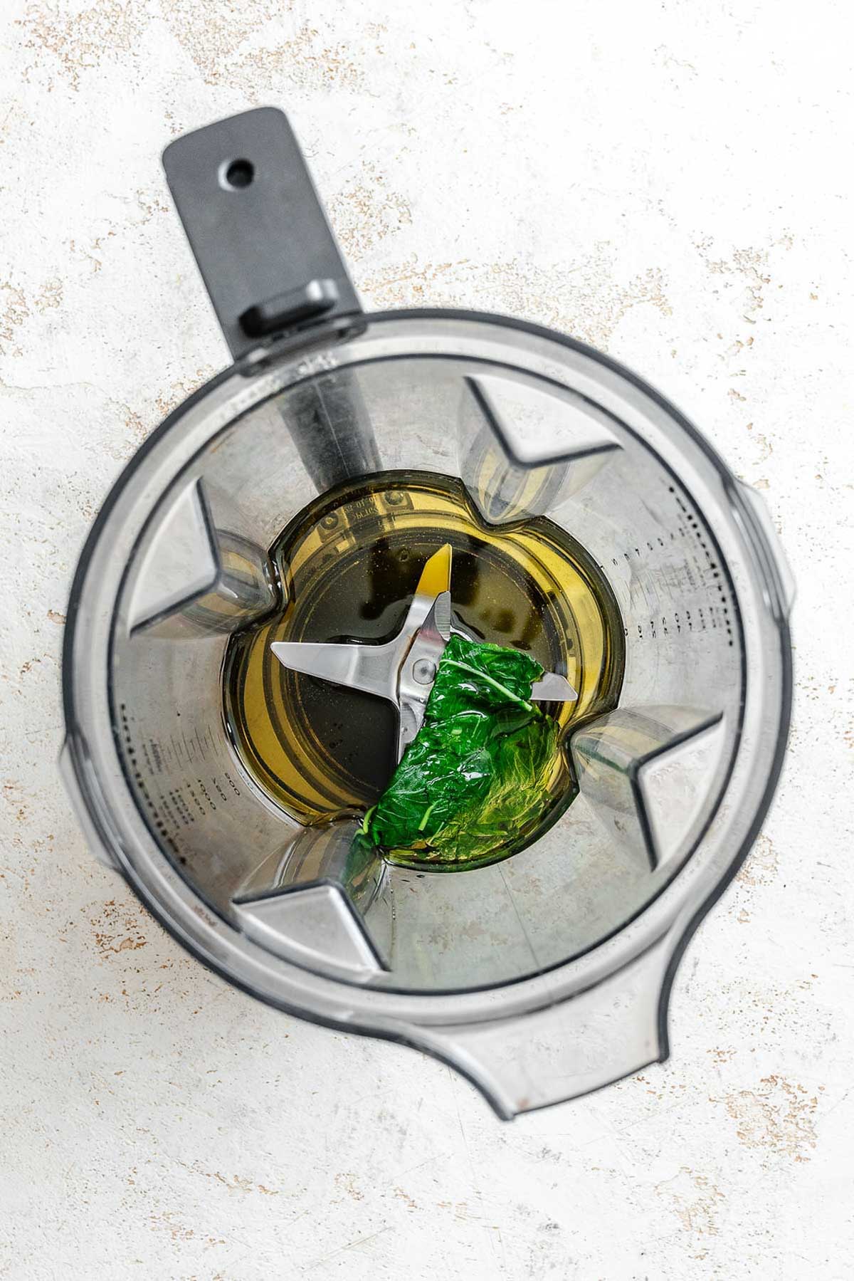 Basil and oil in a blender jar, ready to be pureed into aromatic basil oil.