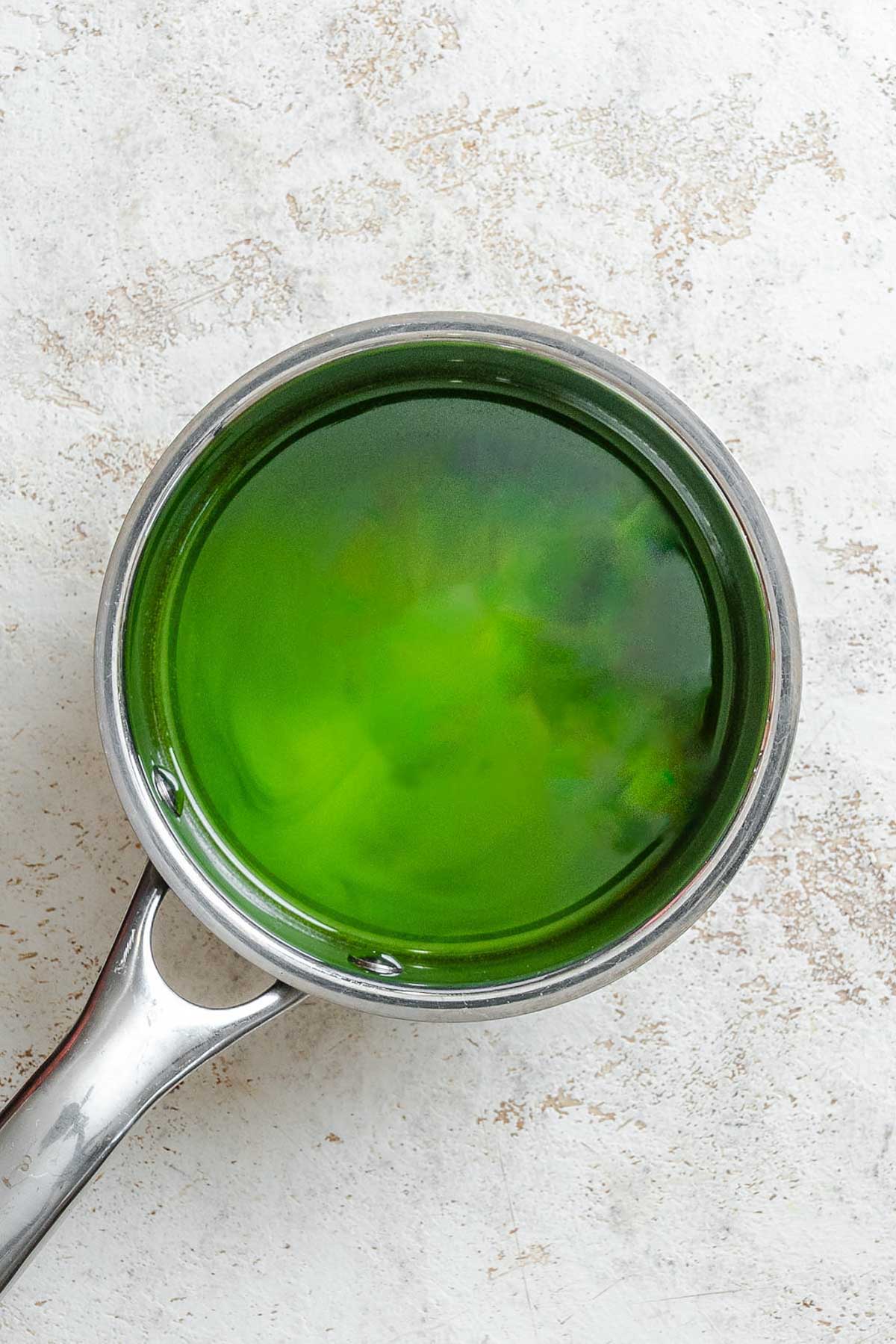 Gently heating strained basil oil in a saucepan until the color turns a deeper, vibrant green.