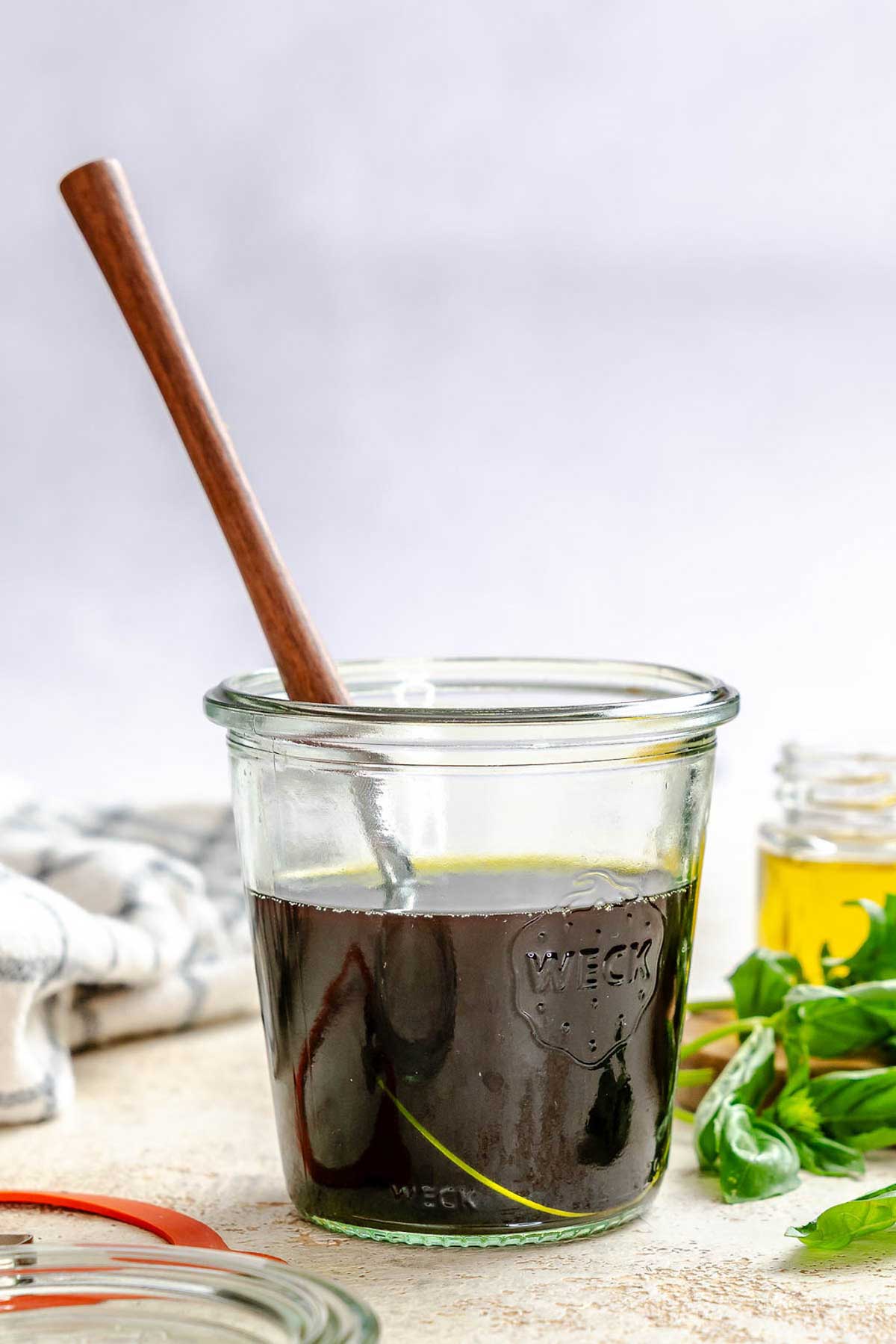 Jar of homemade basil oil with a wooden spoon resting inside, surrounded by fresh basil sprigs.