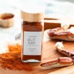 Homemade Old Bay seasoning spilling onto a wood board next to crab claws and newspaper, styled for a classic crab feast setting.