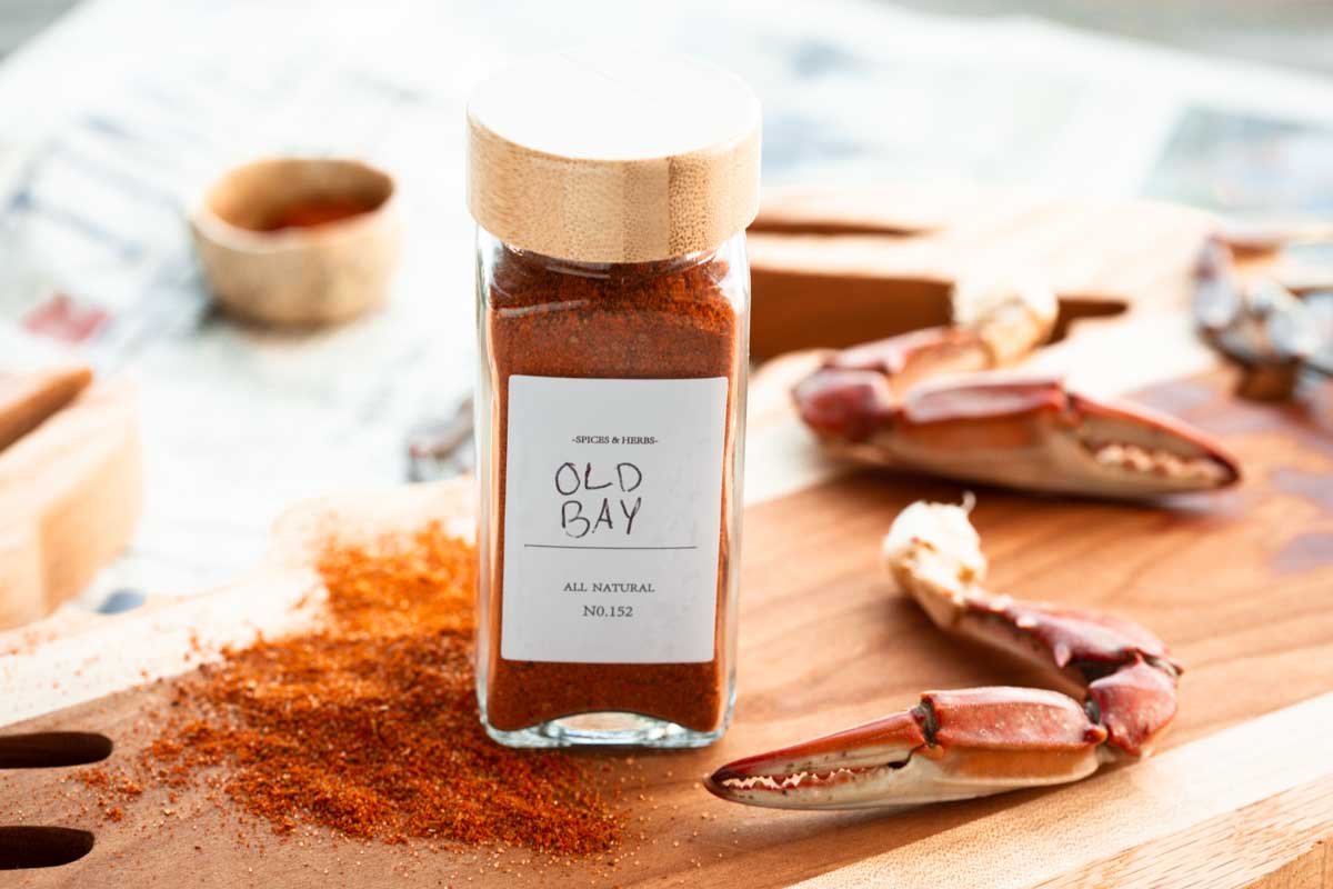 Homemade Old Bay seasoning spilling onto a wood board next to crab claws and newspaper, styled for a classic crab feast setting.