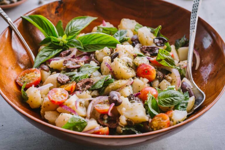 Wide bowl of insalata pantesca – A large serving of Sicilian potato salad in a wooden bowl, with bright basil leaves and glossy cherry tomatoes.