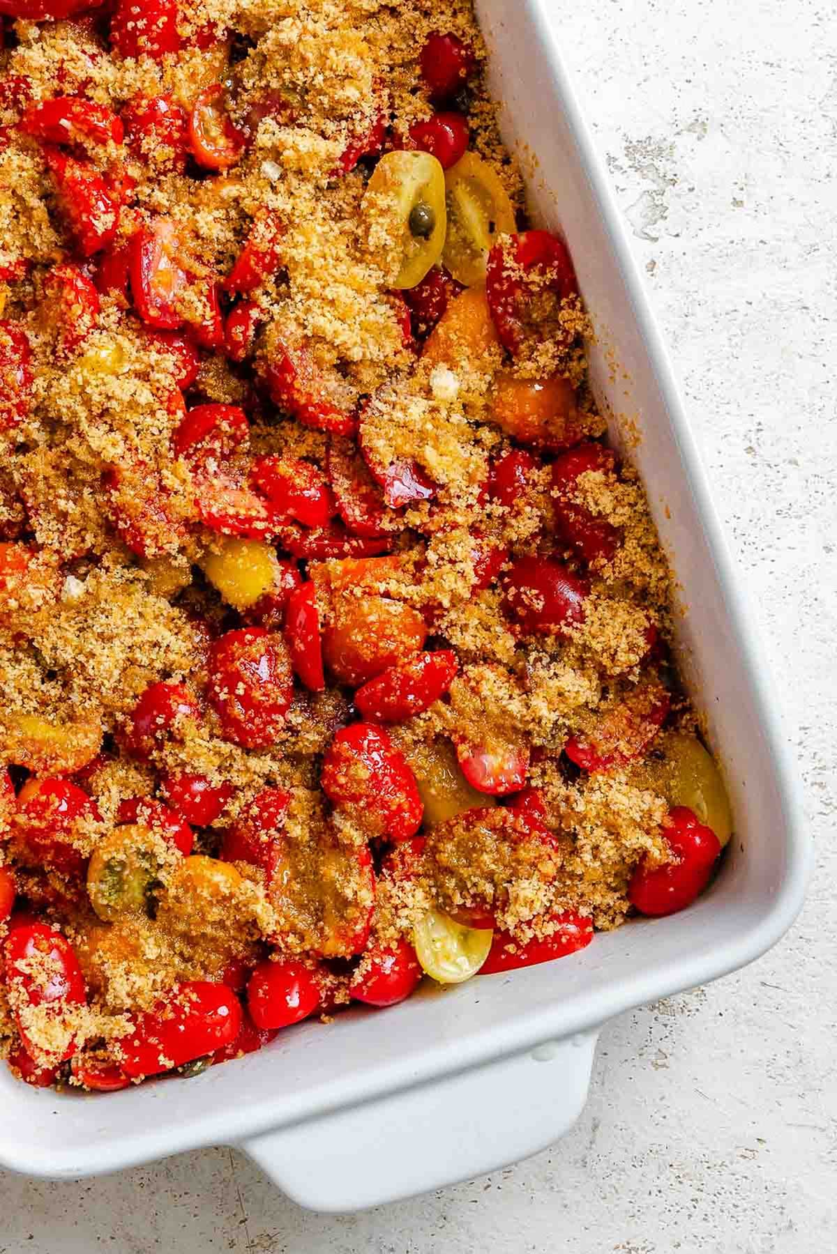 Tomato and caper mixture topped with golden breadcrumbs in a white baking dish before baking.