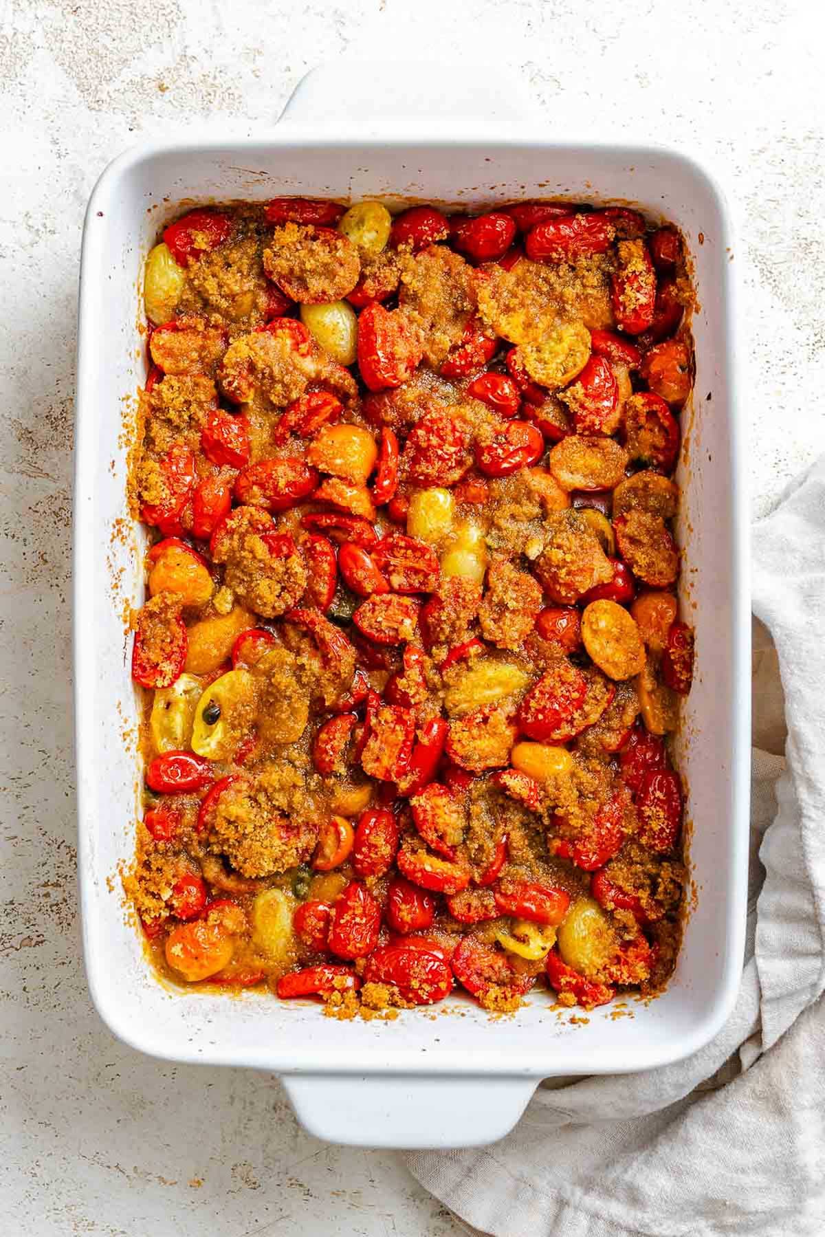 Baked tomatoes and capers with crispy browned breadcrumbs in a white dish, fresh out of the oven.