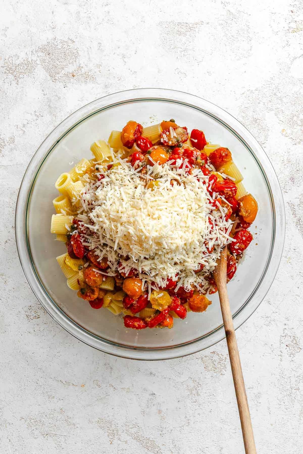 Rigatoni pasta topped with a generous pile of grated cheese over baked tomatoes and capers.