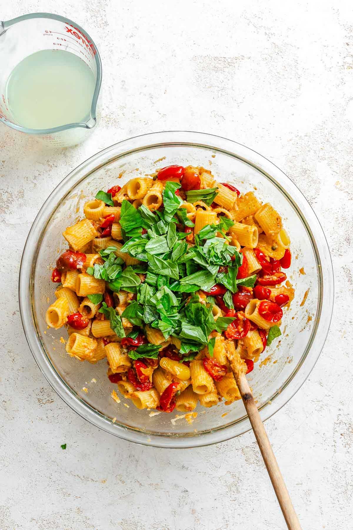 Rigatoni pasta tossed with baked tomatoes, capers, cheese, and topped with fresh basil leaves.