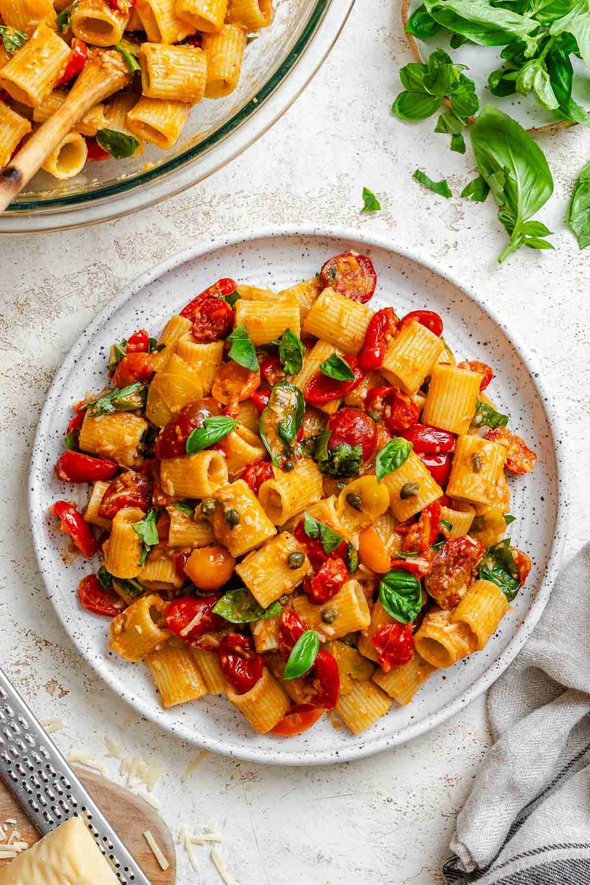 Close-up overhead view of Pasta Ponza plated with rigatoni, tomatoes, capers, basil, and breadcrumbs.
