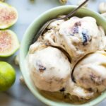 A close-up of three scoops of ricotta, pistachio and fig gelato in a green bowl with visible swirls of roasted figs, fresh figs and pistachios arranged around.