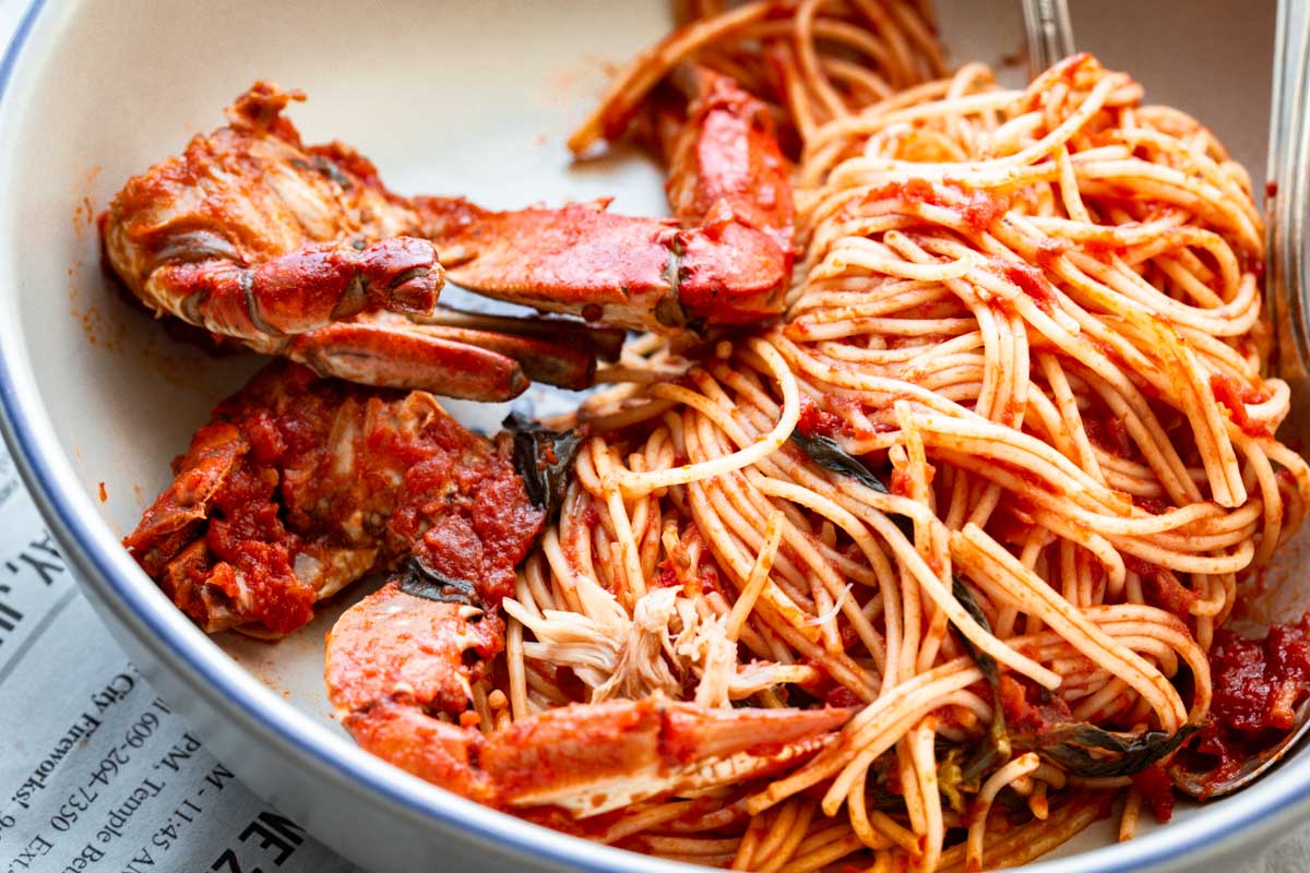 Close-up of spaghetti tangled with crab meat and claws in red sauce, highlighting texture and sheen.