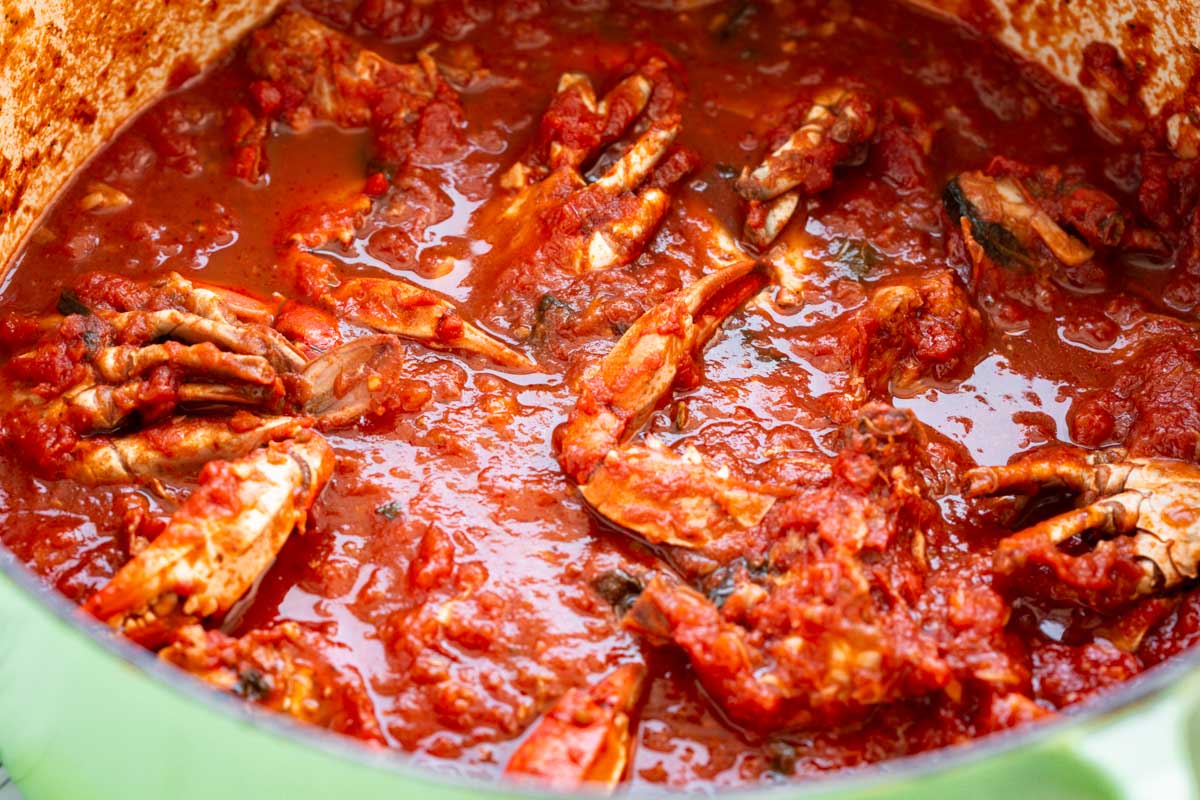 Large green Dutch oven filled with crabs simmering in a chunky tomato sauce.