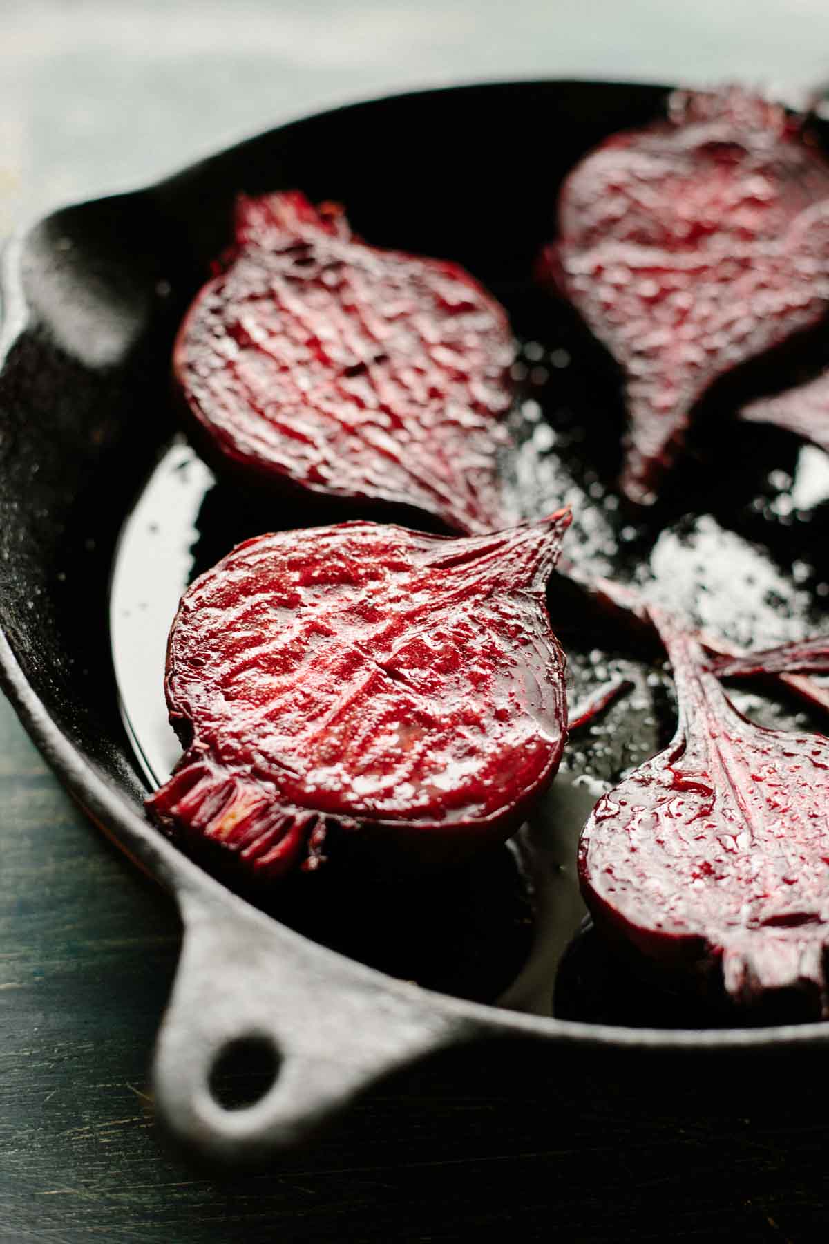 Close-up of glossy, halved roasted beets in a cast iron skillet, glistening with olive oil and lightly charred on the surface.