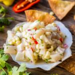 Scallop ceviche served in a scallop shell with crispy tortilla chips and sliced pepper in the background.