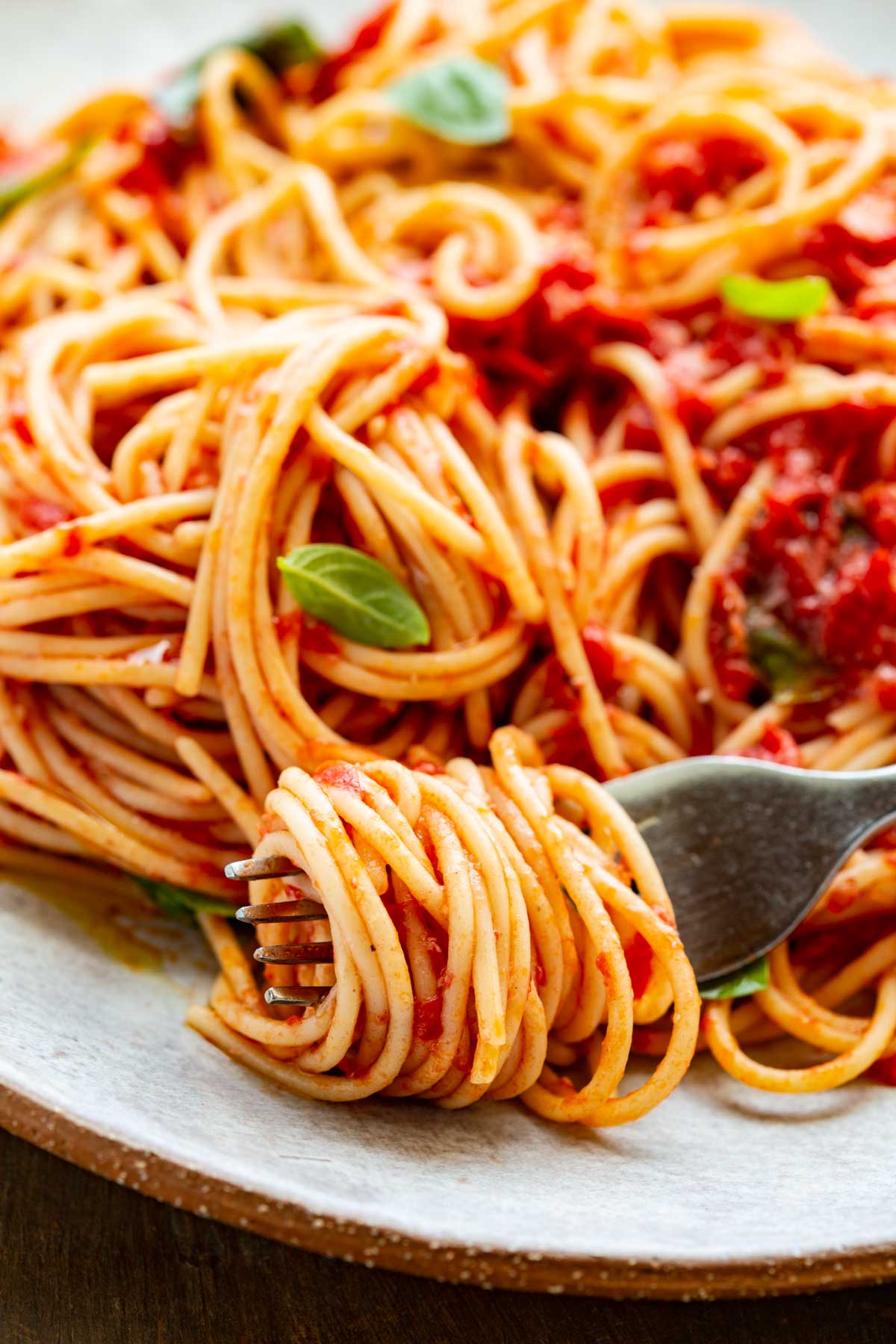 Close-up of spaghetti twirled on a fork - Golden strands of spaghetti coated in fresh tomato sauce, wrapped around a fork with small basil leaves peeking through.