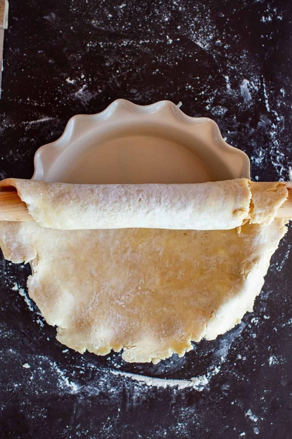 Rolling out flaky pie dough to fit in a pie dish.