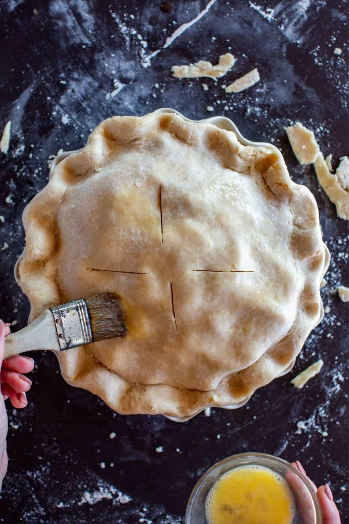 Hand brushing the top of old fashioned apple pie with egg wash.