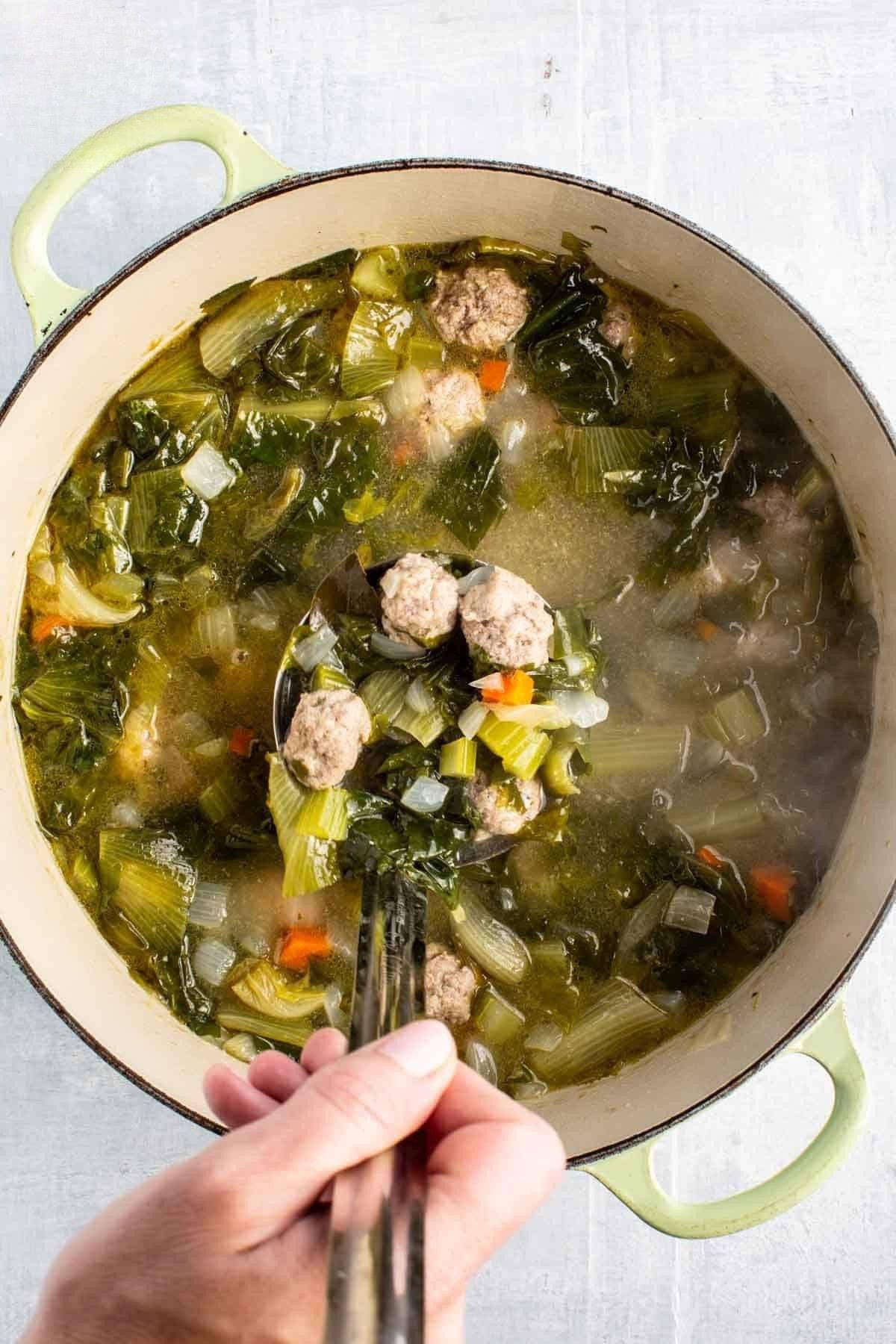 A ladle full of Italian wedding soup in a Dutch oven.