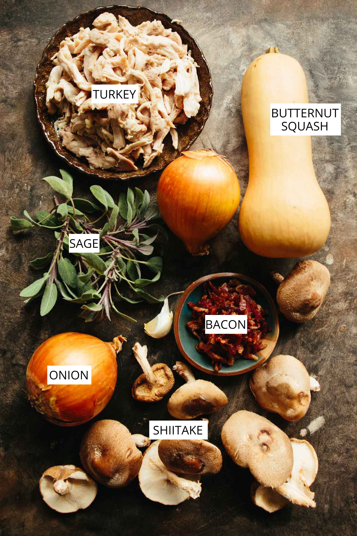 Overhead photo of raw ingredients for mini turkey pot pies, including shredded turkey, a whole butternut squash, onions, fresh sage, shiitake mushrooms, garlic, and a small dish of crisped bacon.