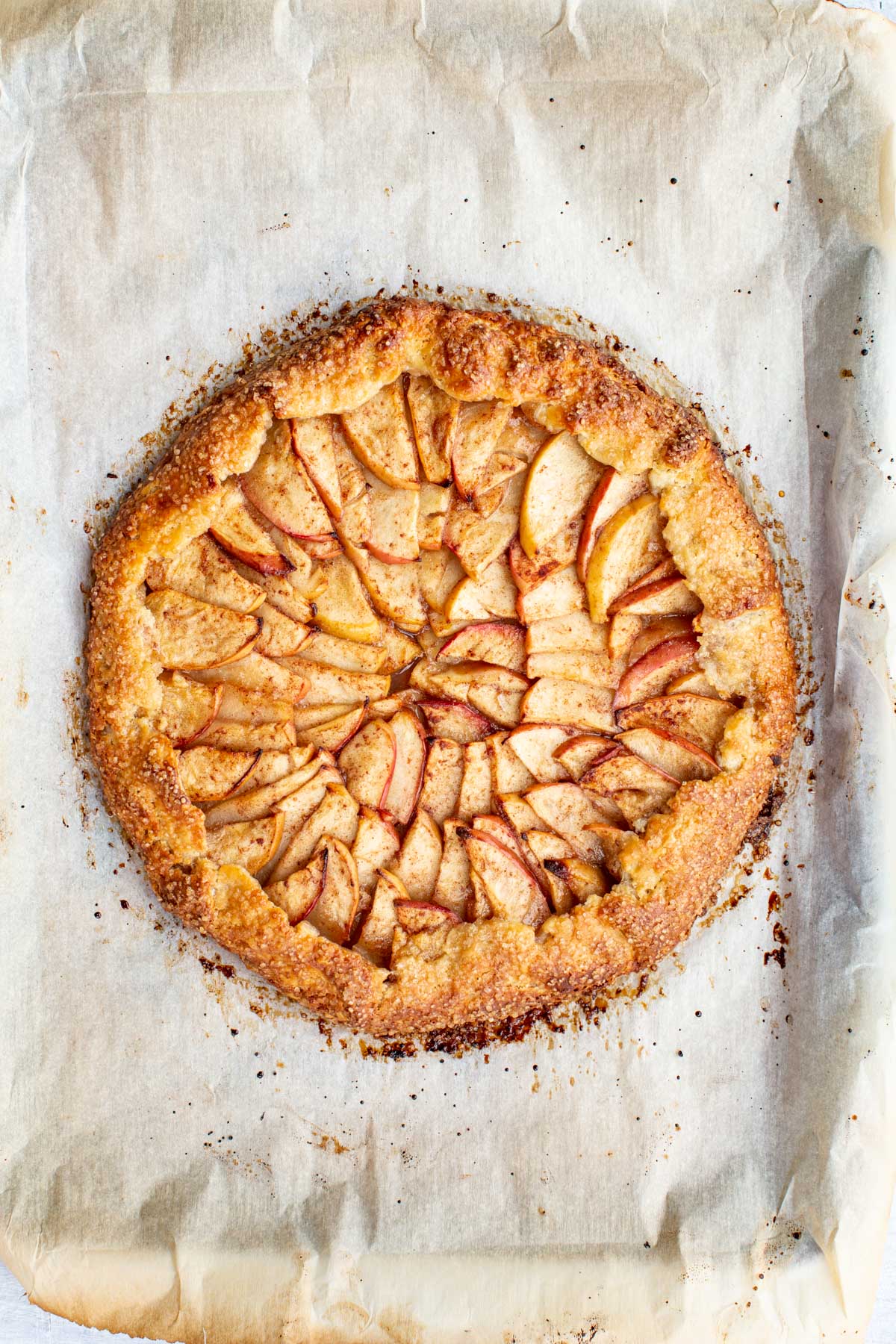 A golden brown apple crostata baked on parchment paper, showing rustic folded edges and neatly arranged apple slices in concentric circles.