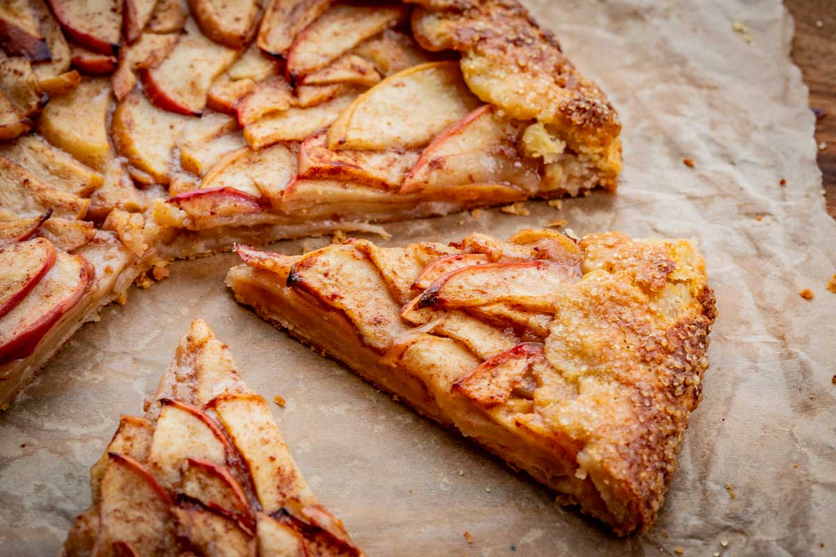 Slices of apple crostata cut from the tart on parchment paper, showing tender layers of baked apples and a crisp, sugar-coated crust.