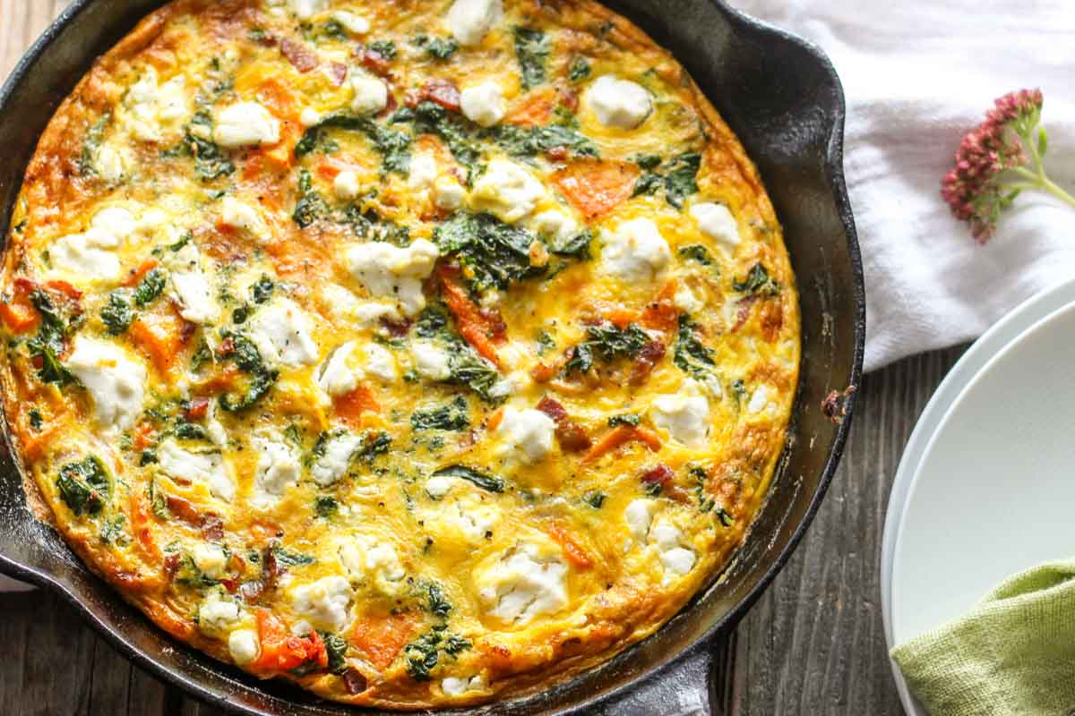 Overhead view of whole butternut squash frittata - A rustic cast iron pan on a wooden table with a browned, cheesy egg surface.
