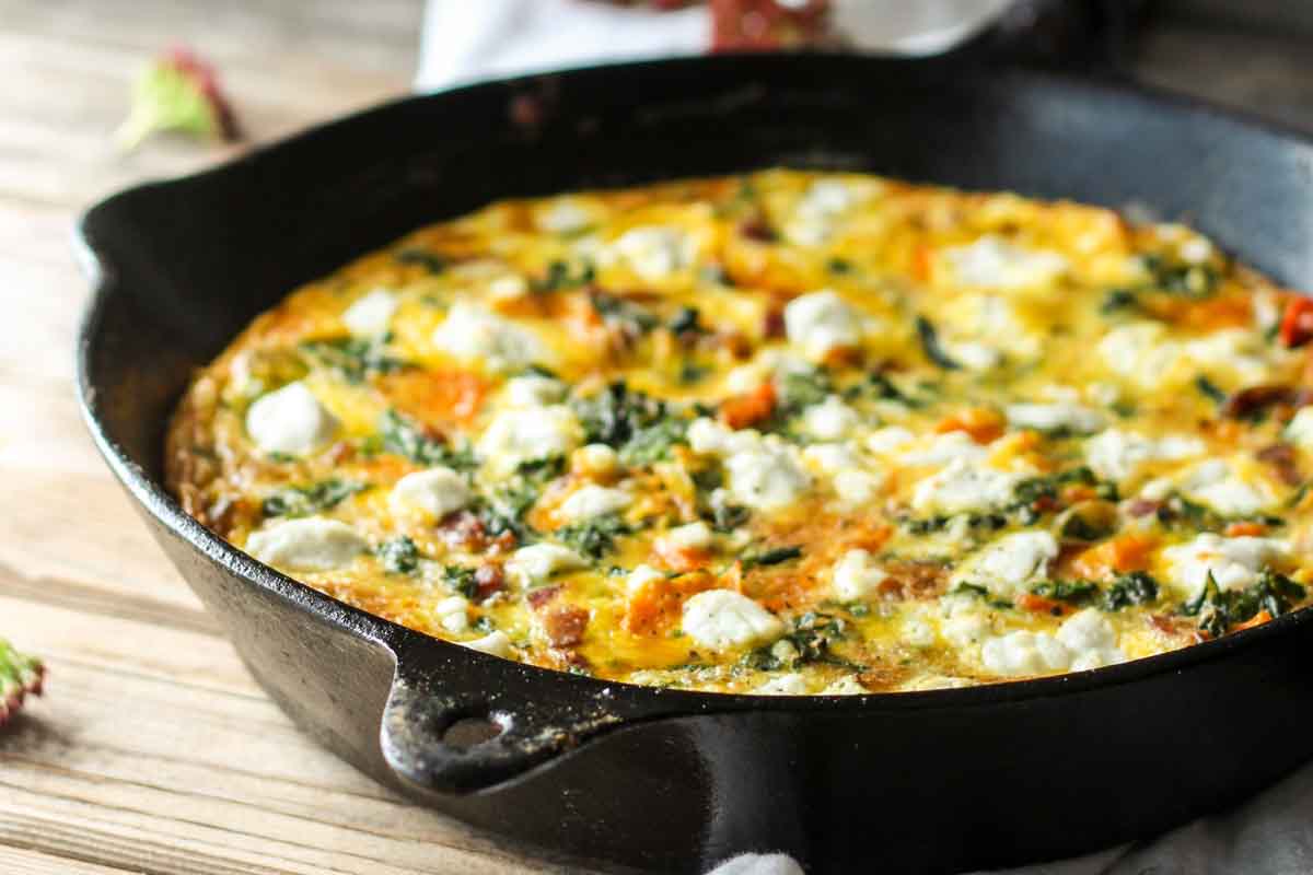 Side view of whole baked frittata in skillet – A rustic presentation with a puffed golden surface topped with creamy goat cheese and greens.