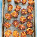 A full baking sheet lined with a wire rack, filled with evenly cooked fritters, their lacy edges crisp and deeply golden.