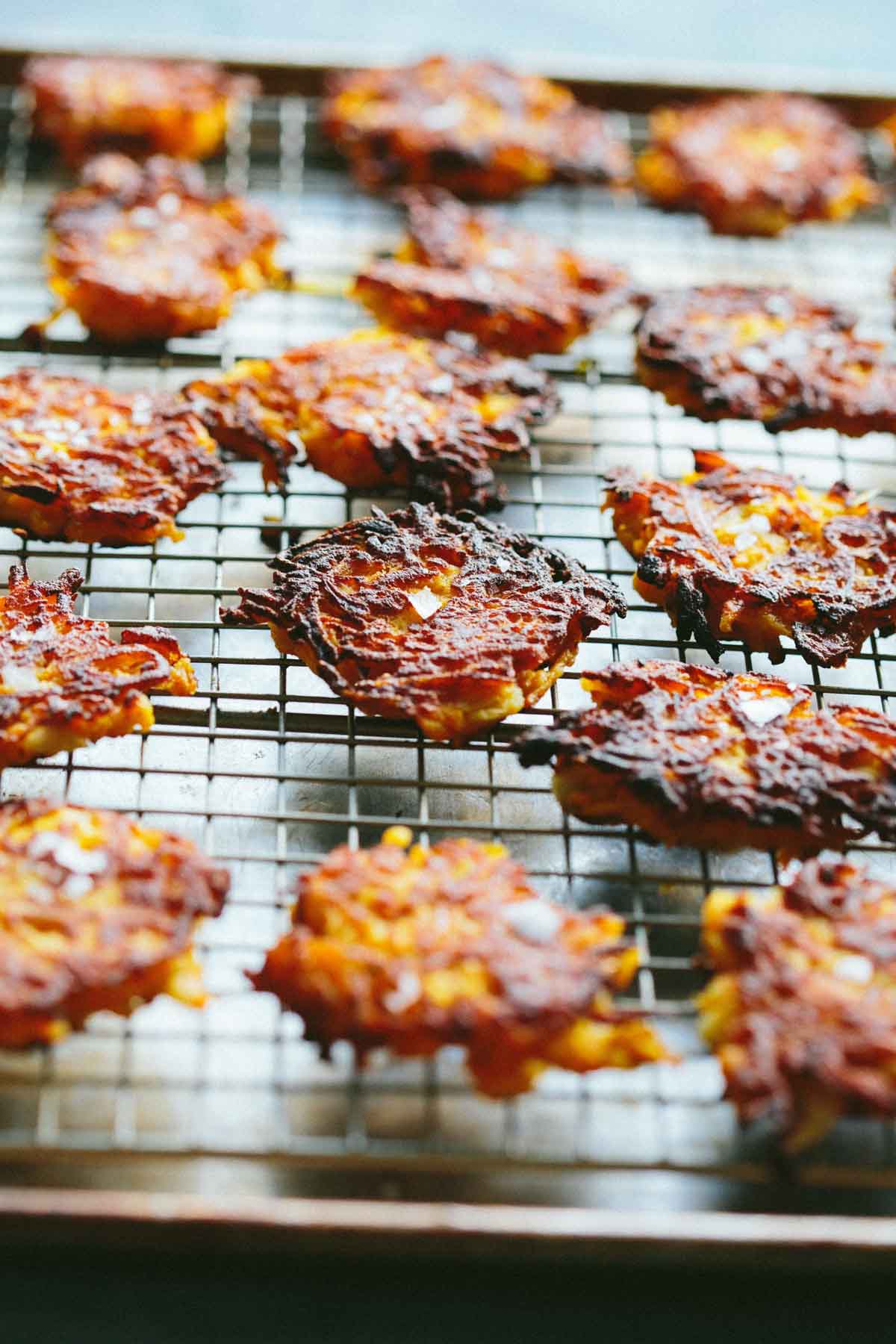 Crispy golden brown butternut squash fritters resting on a wire rack, showing caramelized edges and flaky salt sprinkled on top.