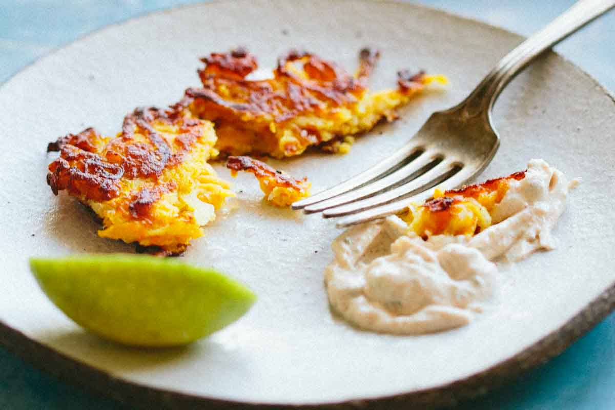 Close-up of golden fritters on a plate beside a fork, creamy spiced yogurt, and a fresh lime wedge.