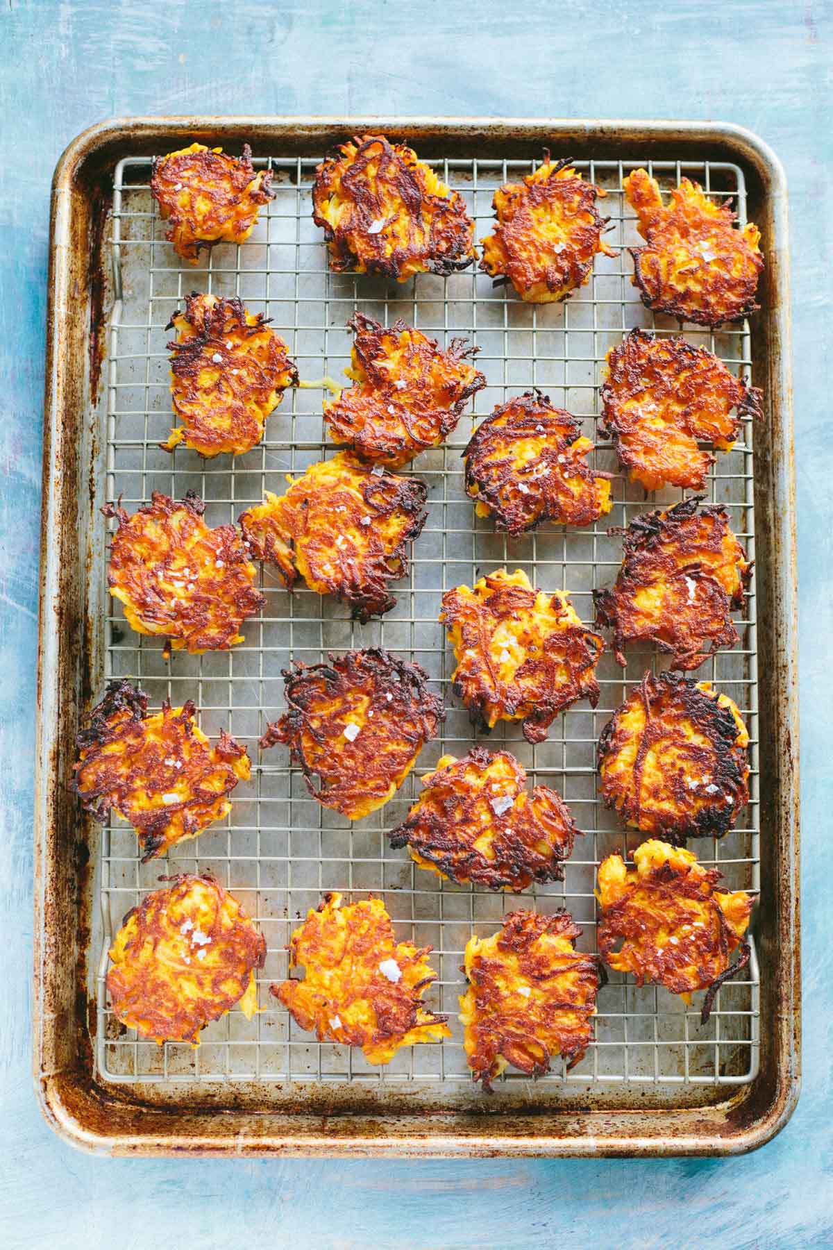 A full baking sheet lined with a wire rack, filled with evenly cooked fritters, their lacy edges crisp and deeply golden.