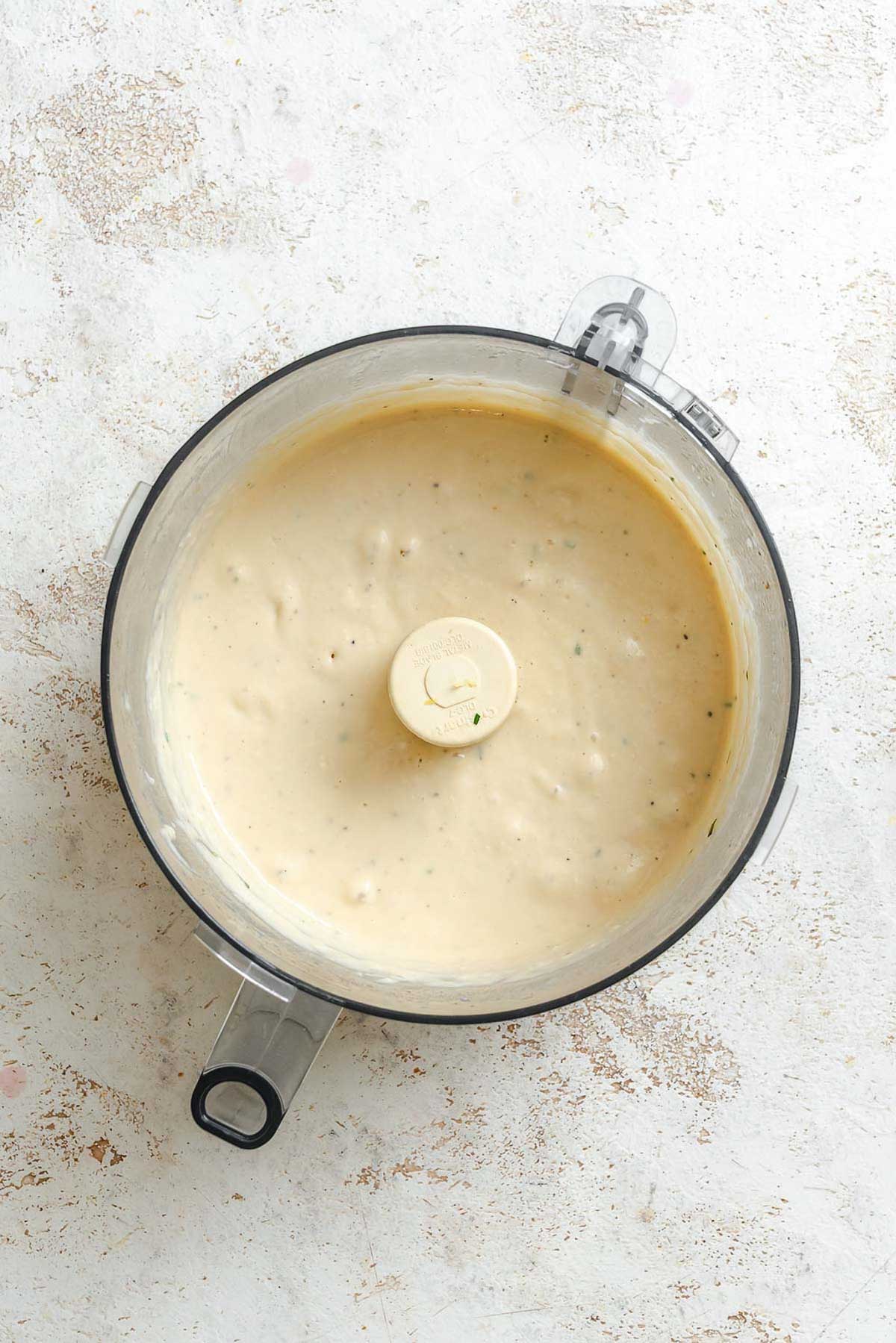 Smooth and blended white bean dip filling the bowl of a food processor, showing a creamy, uniform texture.
