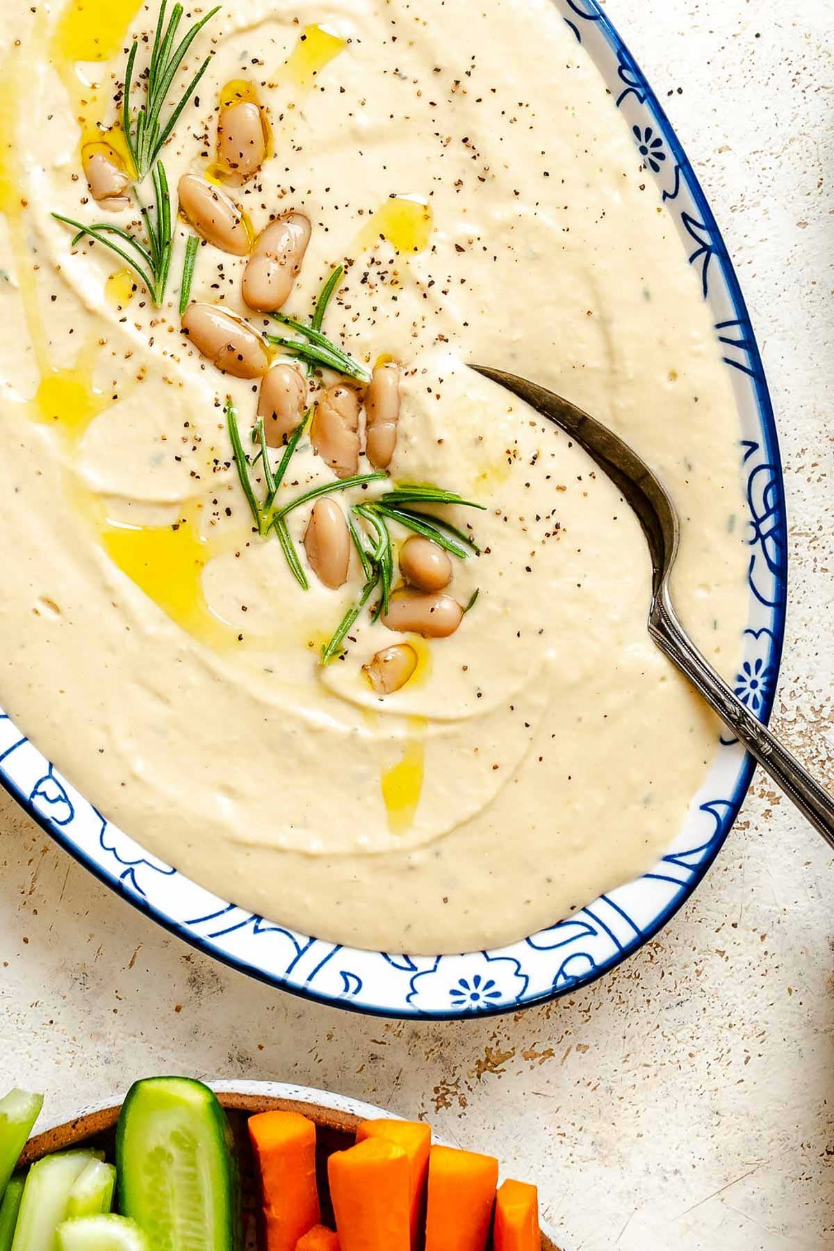 Close-up of the dip's surface, showing garnishes of rosemary, beans, olive oil, and black pepper.