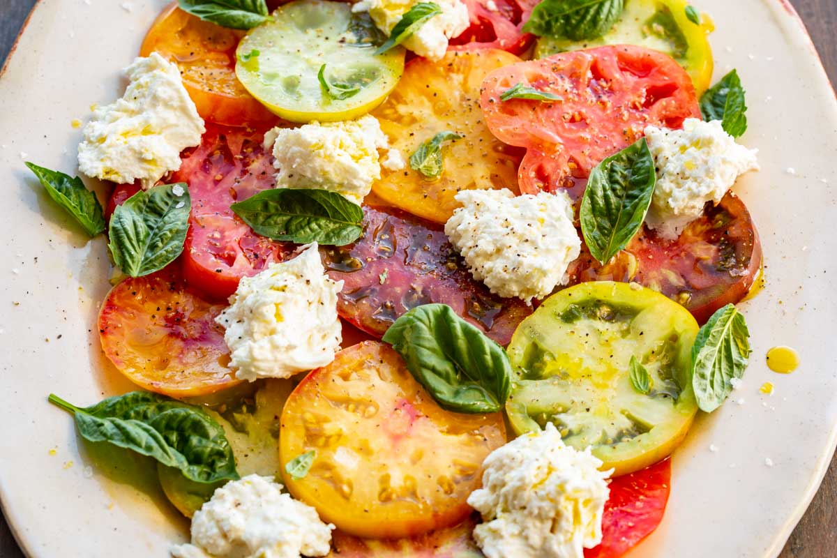 Finished Caprese salad on a platter with colorful heirloom tomato slices, mozzarella chunks, and fresh basil leaves.