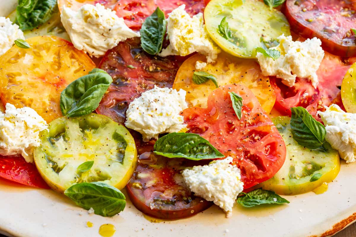 Close-up side view of Caprese salad highlighting olive oil drizzled over tomatoes, mozzarella, and basil.