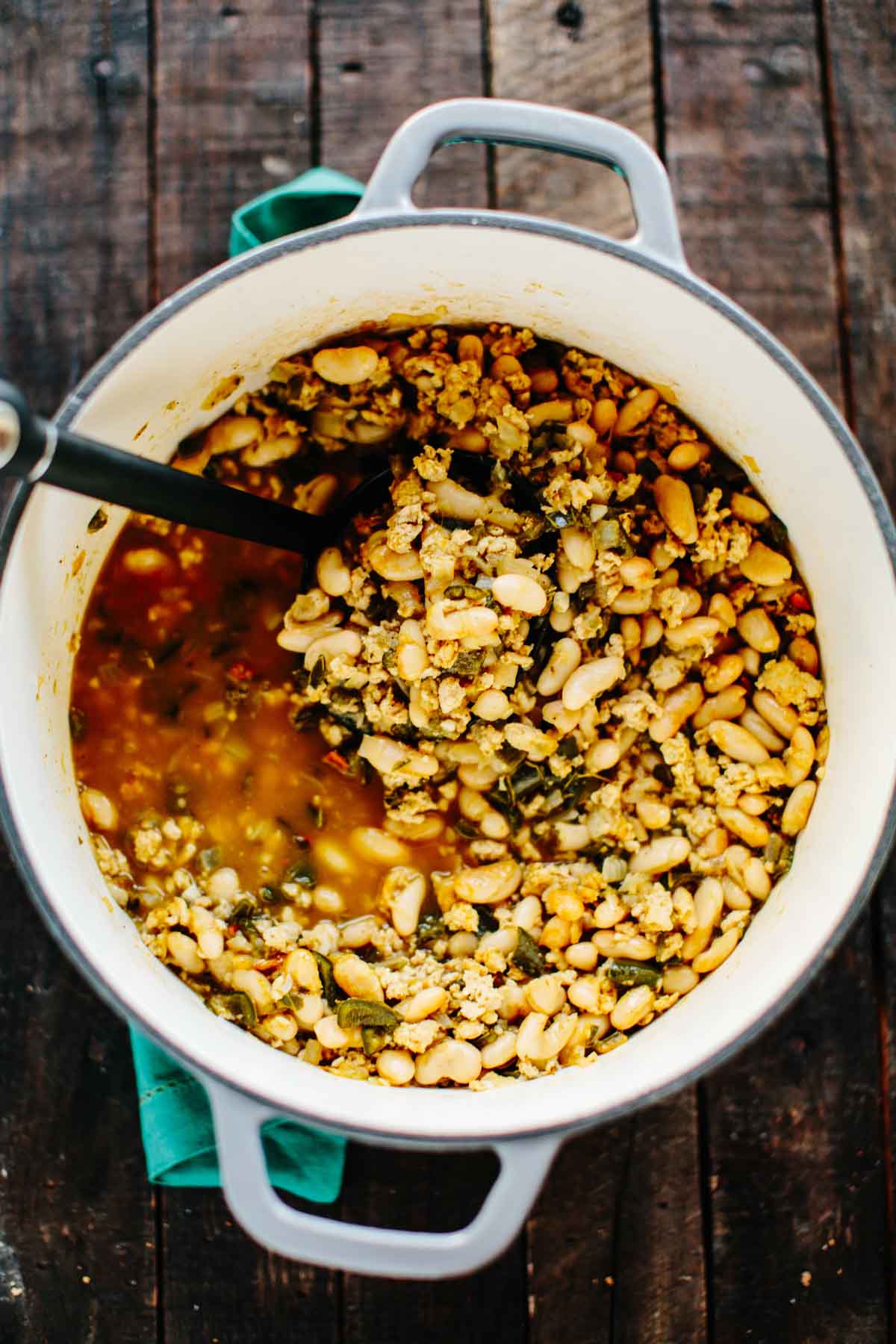 A Dutch oven filled with chicken poblano white bean chili with tender chicken, white beans, poblano peppers, and a spiced broth being ladled out.