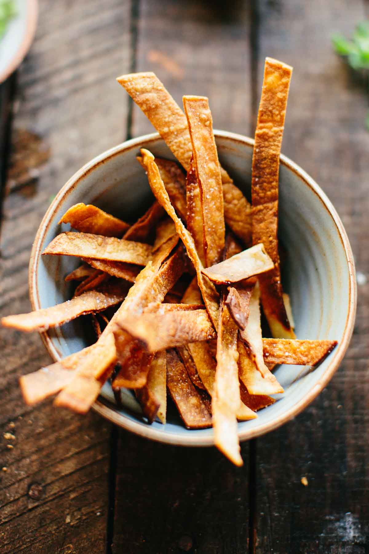 A ceramic bowl filled with golden brown fried tortilla strips ready to serve as a crunchy topping for chili.