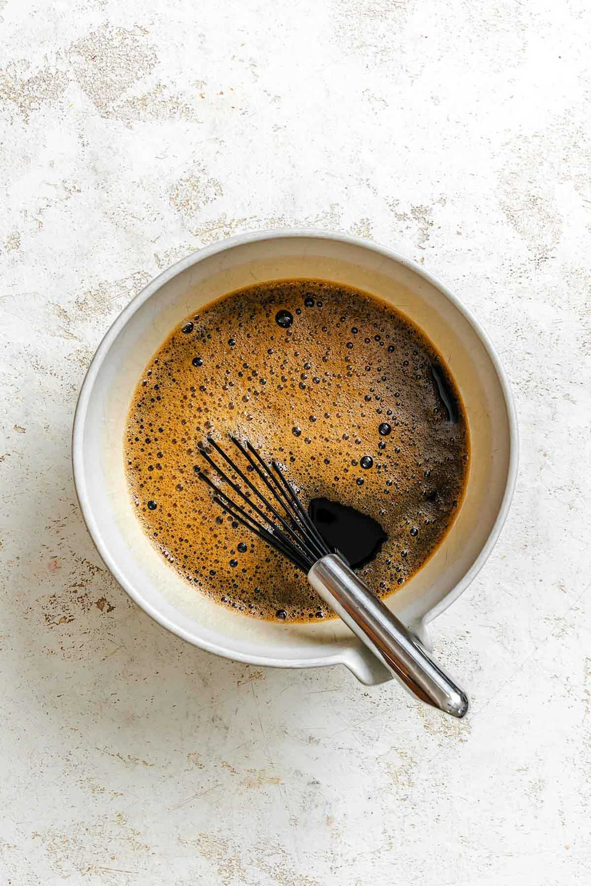 Mixing bowl filled with dark coffee and sugar being whisked together until dissolved.