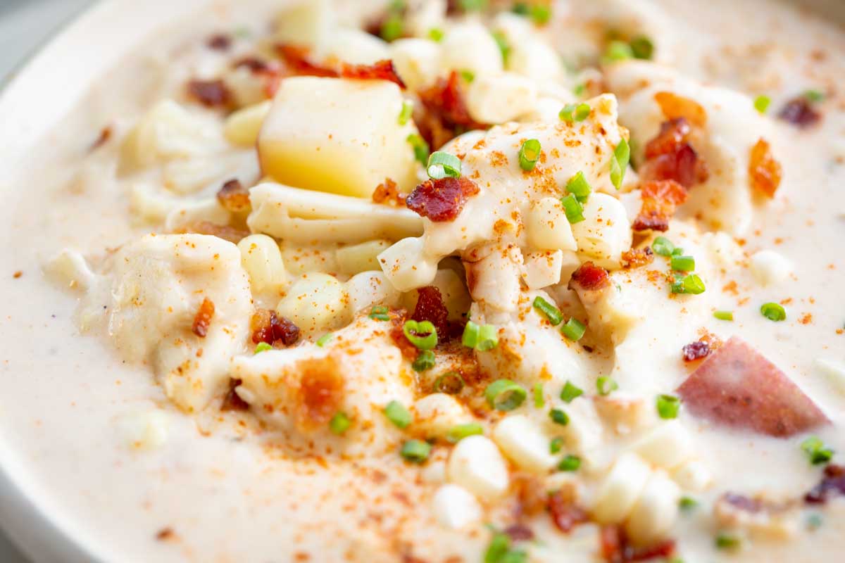 Tight shot of corn and crab chowder highlighting the ingredients-tender potatoes, sweet corn kernels, crab meat, and bacon-sprinkled with chives and Old Bay seasoning.
