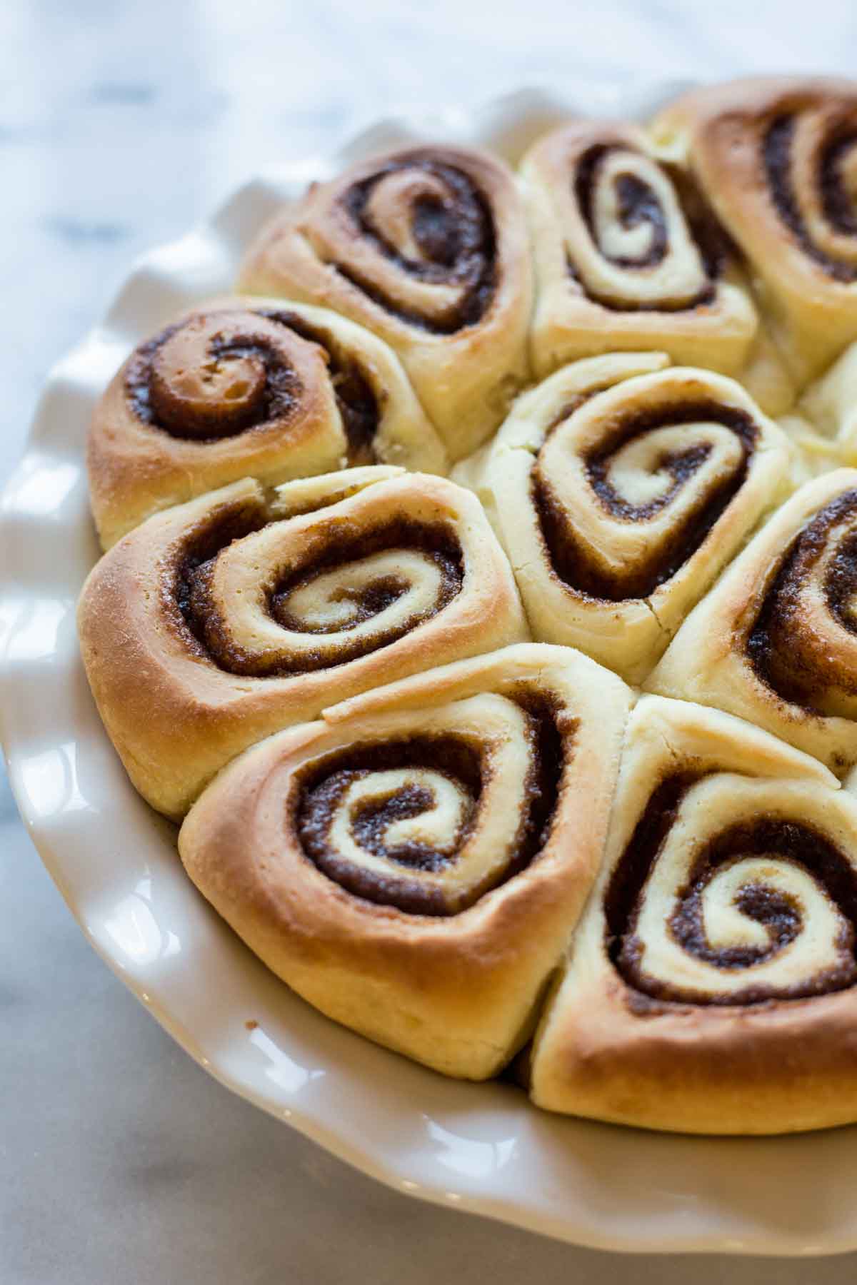 Golden-brown cinnamon rolls baked in a round white pie dish, showing tight spirals of cinnamon sugar filling.