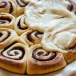 Close-up of warm cinnamon rolls in a pie dish, partially covered in creamy frosting melting into the spirals.