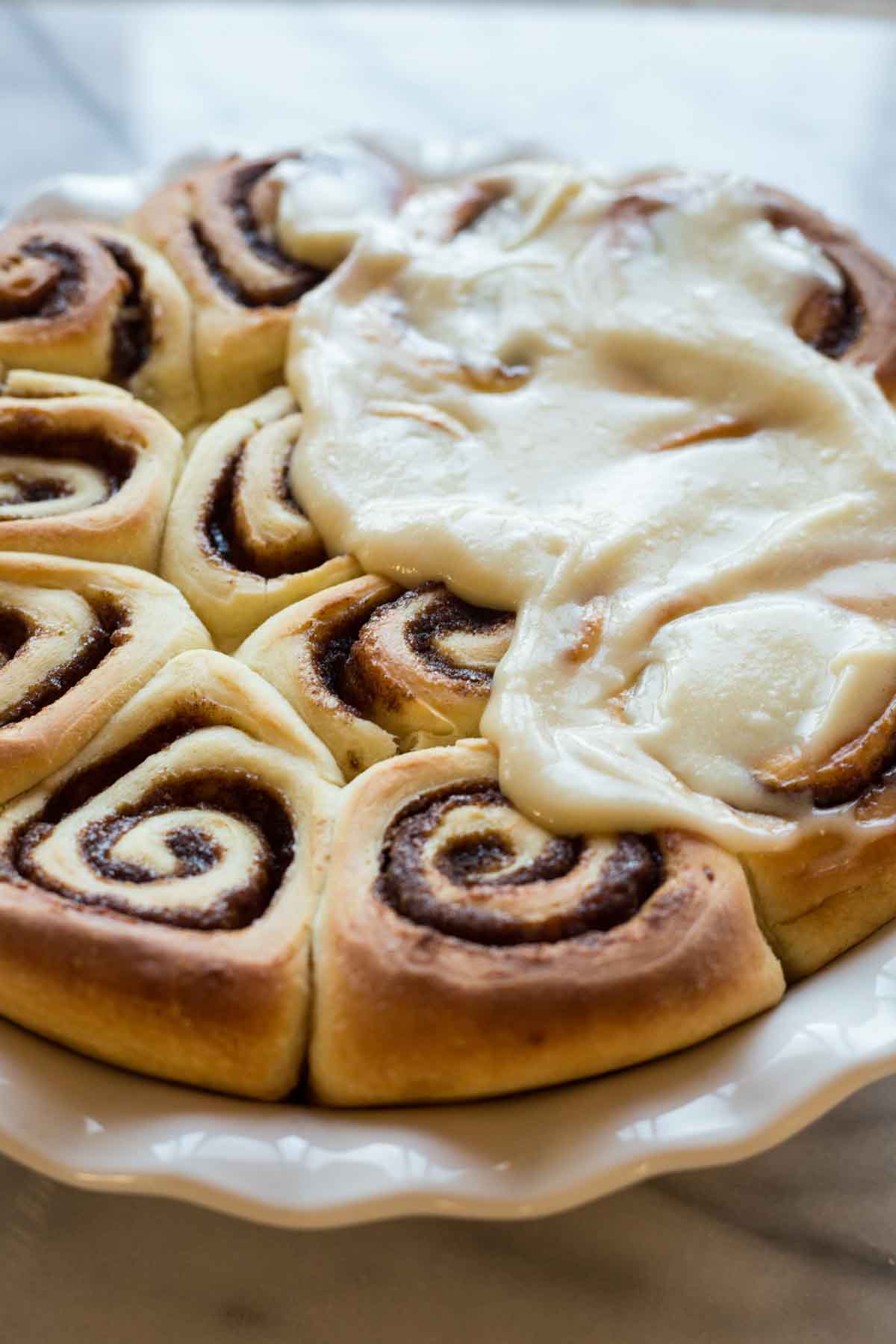 Close-up of warm cinnamon rolls in a pie dish, partially covered in creamy frosting melting into the spirals.
