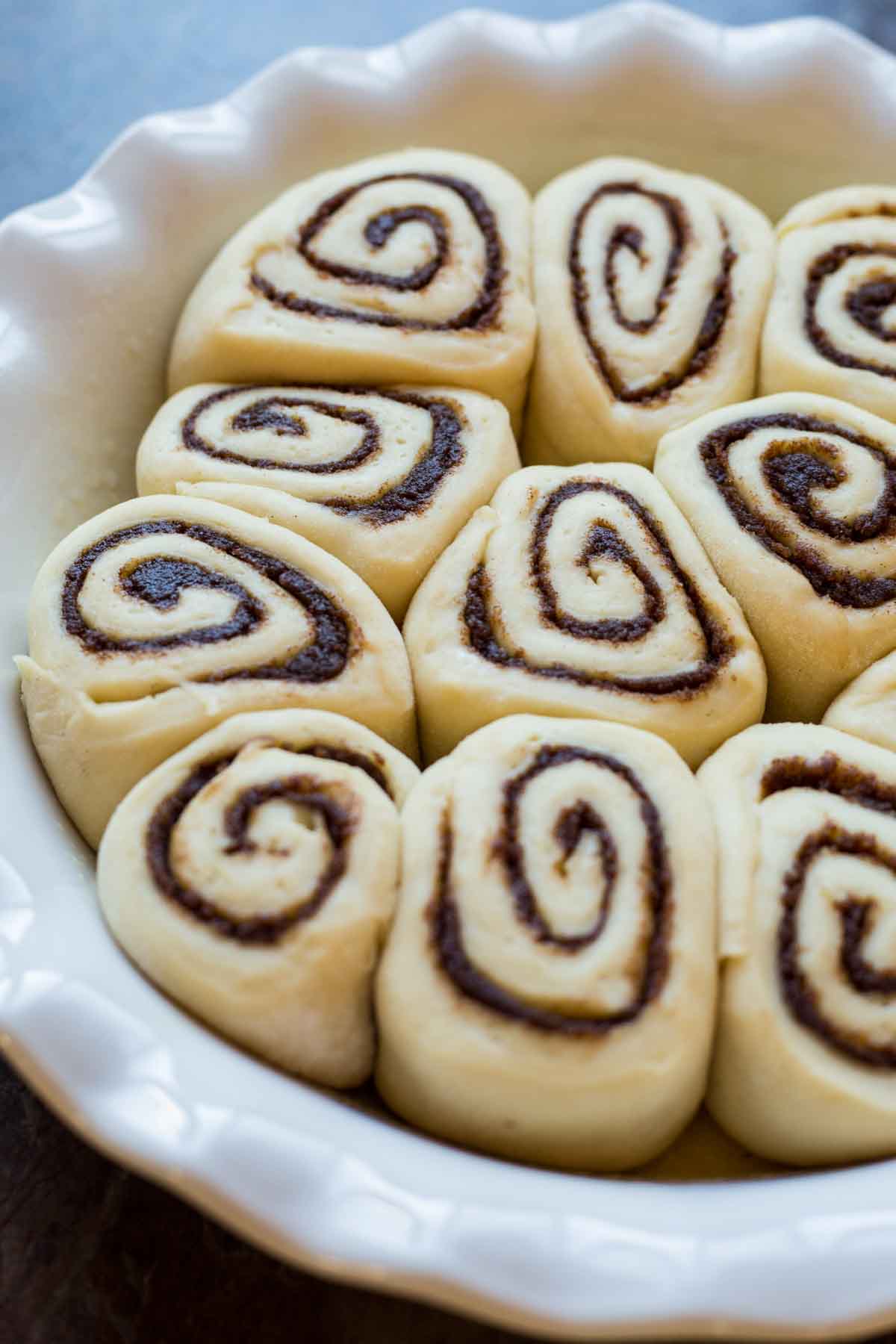 Raw cinnamon rolls arranged in a round white dish, showing neat spirals of cinnamon filling before baking.